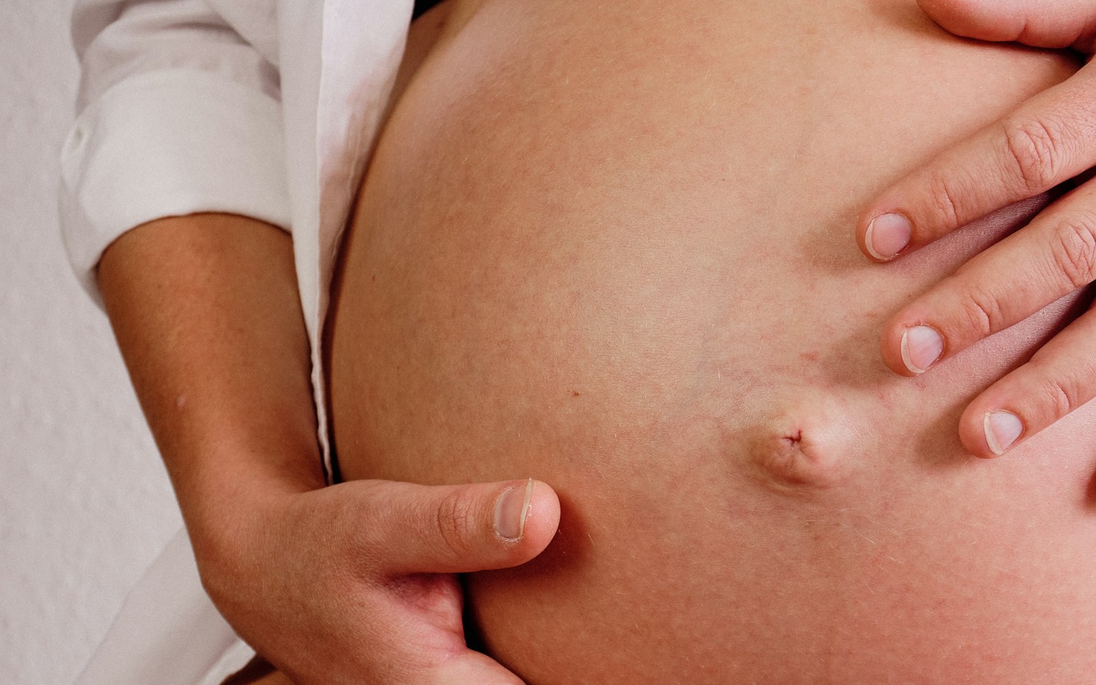 Mains posées avec douceur sur le ventre d'une femme enceinte, geste rassurant, lumière chaude et enveloppante.